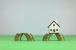 scale model house sitting across stacks of pound coins. financial bridging loan concept.